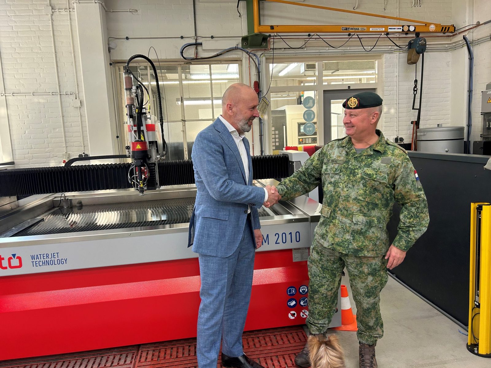 Poignée de main entre un représentant de Resato et un militaire devant la nouvelle machine de découpe au jet d'eau