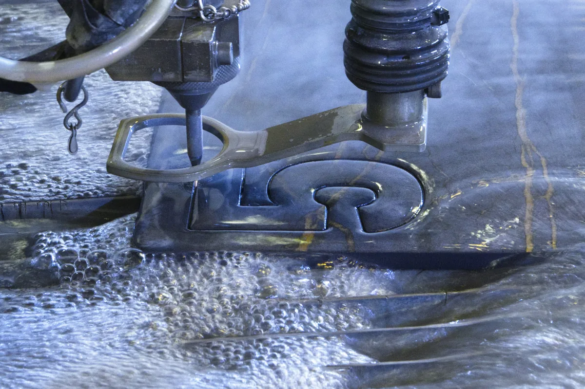 Le jet d'eau découpe une lettre dans une tôle d'acier, le contour presque refermé.