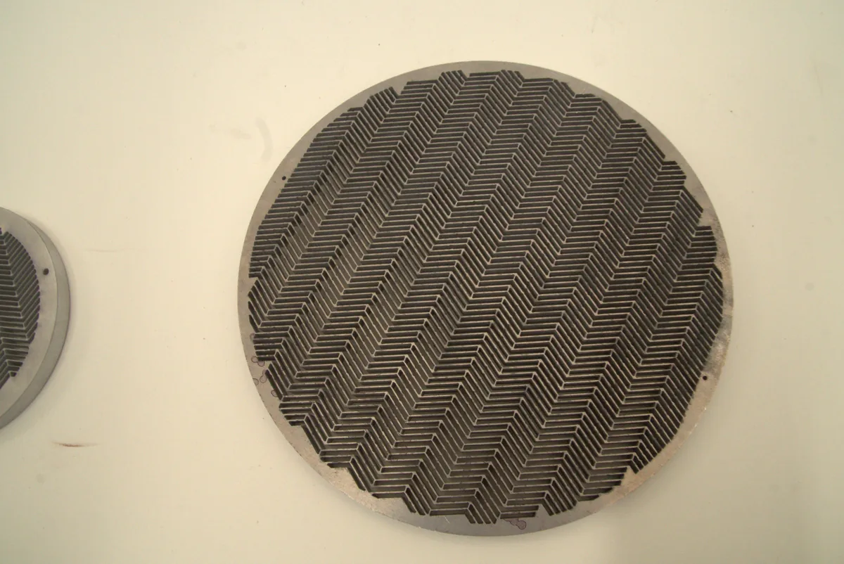 Ronde metalen schijf met een fijn visgraatpatroon van doorlopende sneden.