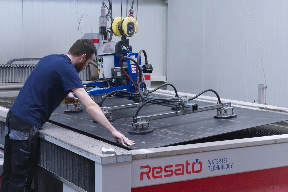 Worker placing a sheet on the cutting table using a crane-mounted vacuum lifter.